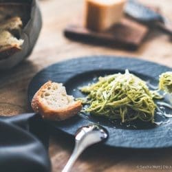 Pesto Spaghetti auf schwarzem Teller mit Brot auf dem Rand