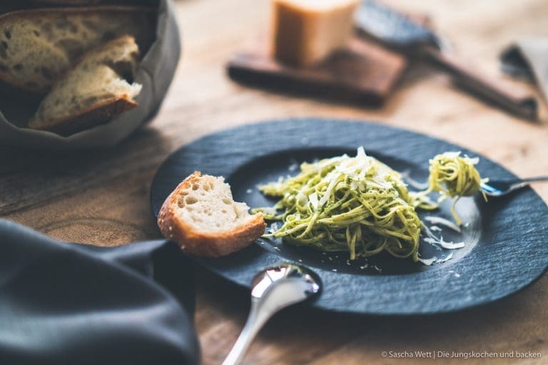 Pesto Spaghetti auf schwarzem Teller mit Brot auf dem Rand