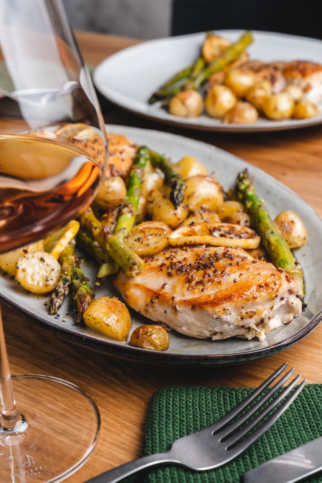 Honig-Senf-Hähnchen vom Blech auf dem Servierteller. Angerichteter Teller im Hintergrund