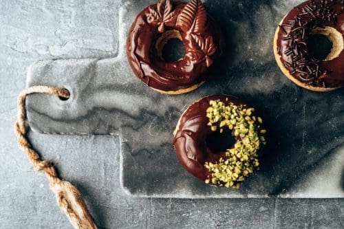 Vegane Schoko Donuts 5 | Wenn es Euch so geht wie uns, sind die einzigen veganen Donuts, die Ihr bisher kanntet, trocken und geschmacklos. Daher mussten wir uns einfach an einem eigenen veganen Rezept für saftige Donuts austesten! Wir probieren ja  ständig neue Rezepte aus und entdecken interessante Dinge im Supermarkt. Daher geht es heute auch um Schokoladenglasur - unsere Lieblingsglasur. Wir haben uns so richtig bei der Verzierung der veganen Donuts ausgetobt und sie waren ein solcher Erfolg, dass uns jetzt jeder nach diesem einfachen Rezept fragt.