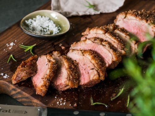 Knusprige Entenbrust aus der Heißluftfritteuse. Komplette Brust aufgeschnitten auf dem Brett und mit Salz bestreut. Rosa glänzendes Brustfleisch.