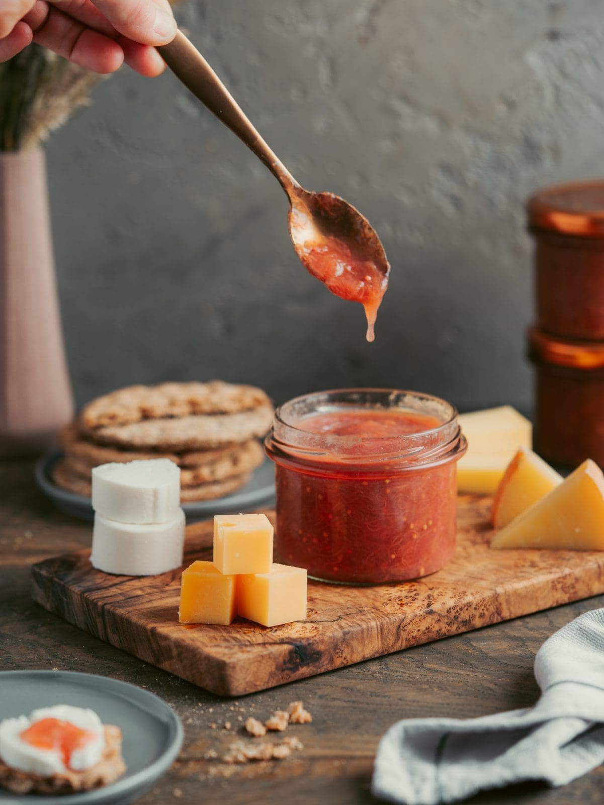 Rhabarber-Chutney im Glas auf dem Brett dekoriert mit Käse und Gebäck. Löffel mit etwas Chutney