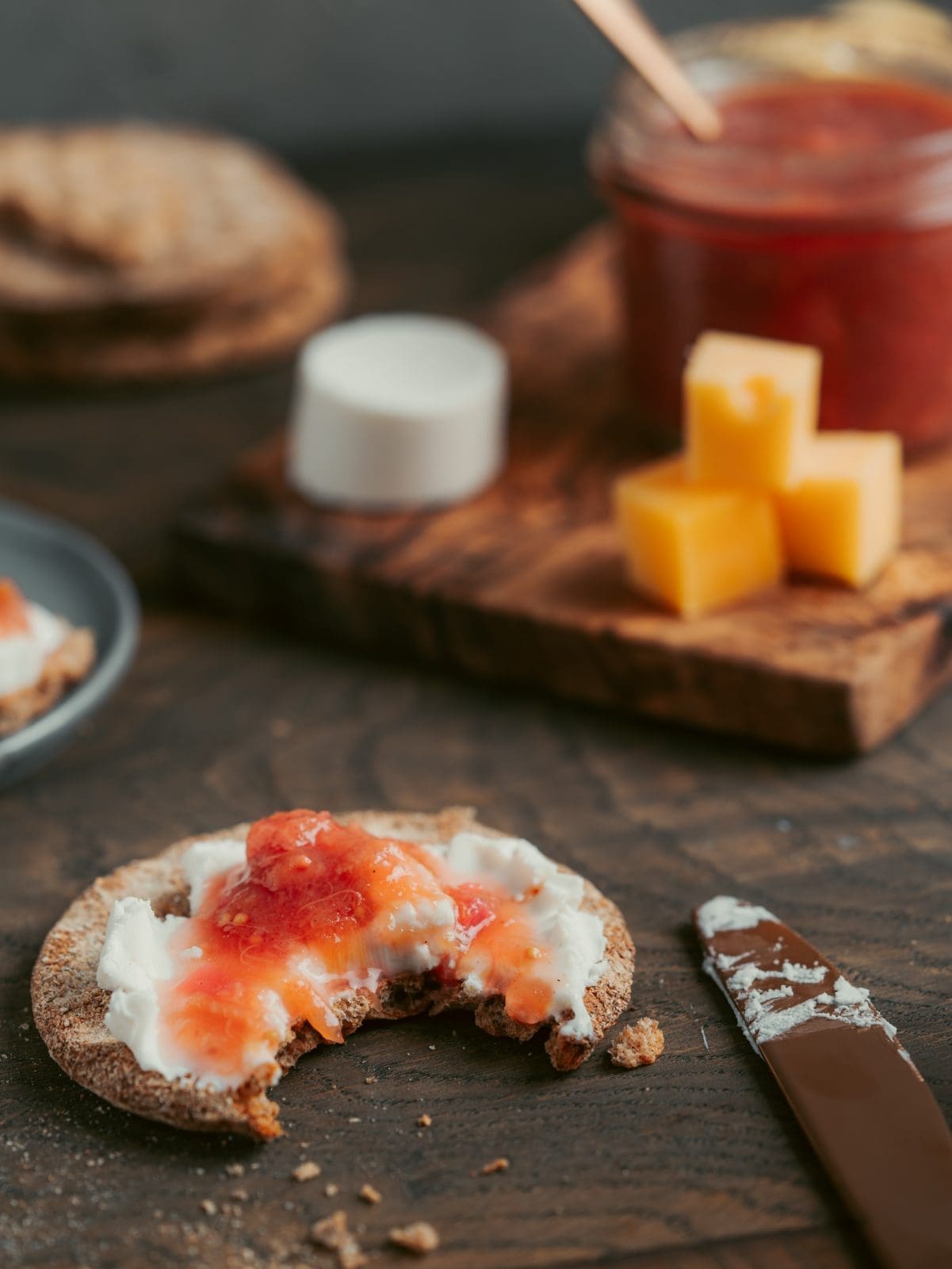Rhabarber-Chutney im Glas auf dem Brett dekoriert mit Käse und Gebäck. Angebissenes Knäckebrot