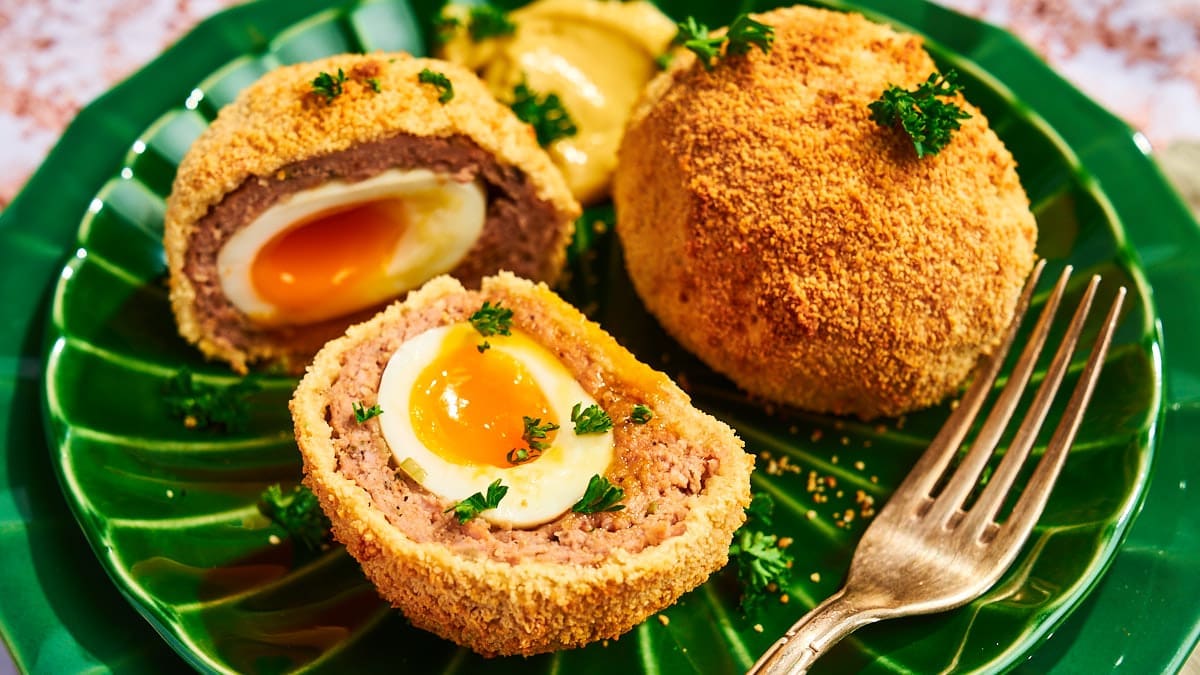 Halbiertes Scotch Egg auf einem grünen Teller mit flüssigem Eigelb und knuspriger Panade, serviert mit Senf.