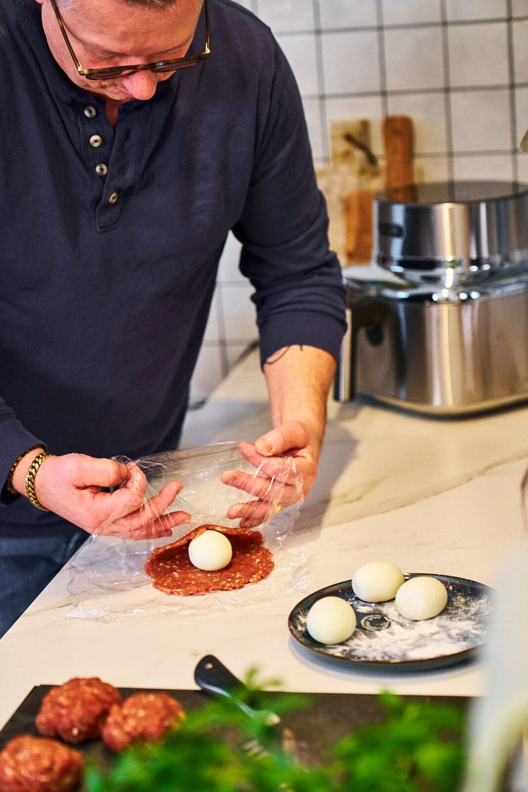 Die Fleischmasse wird mit den Händen gleichmäßig um das bemehlte Ei geformt, sodass eine glatte Kugel entsteht.