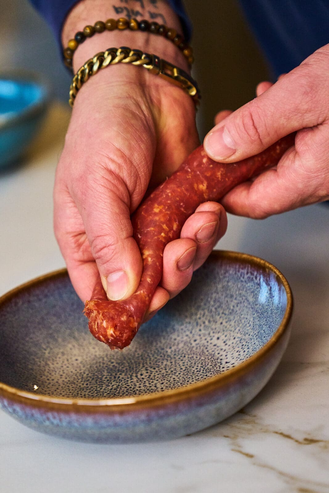 Schritt-für-Schritt Anleitung: Rohes Wurstbrät wird auf Frischhaltefolie flachgedrückt, um ein gekochtes Ei zu ummanteln.