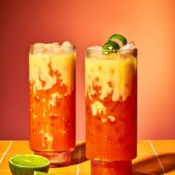 Zwei fertig dekorierte Golden Easter Float Cocktails mit Limettenzeste auf einer orangefarbenen Fliesen-Oberfläche.