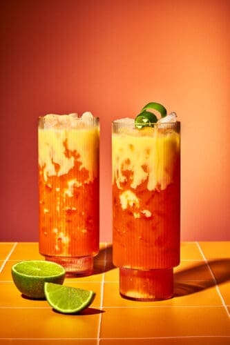 Zwei fertig dekorierte Golden Easter Float Cocktails mit Limettenzeste auf einer orangefarbenen Fliesen-Oberfläche.