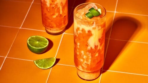 Der ultimative Oster-Cocktail serviert in hohen Rillengläsern auf modernen warm-orangen Kacheln.