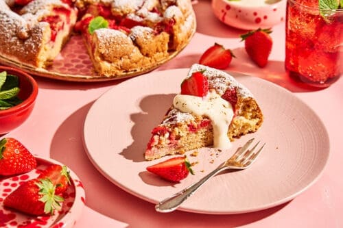 Stück Erdbeerkuchen ohne Butter mit Vanillejoghurt und frischen Erdbeeren auf rosa Untergrund