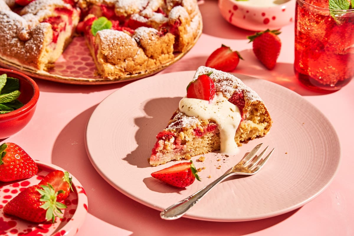 Stück Erdbeerkuchen ohne Butter mit Vanillejoghurt und frischen Erdbeeren auf rosa Untergrund