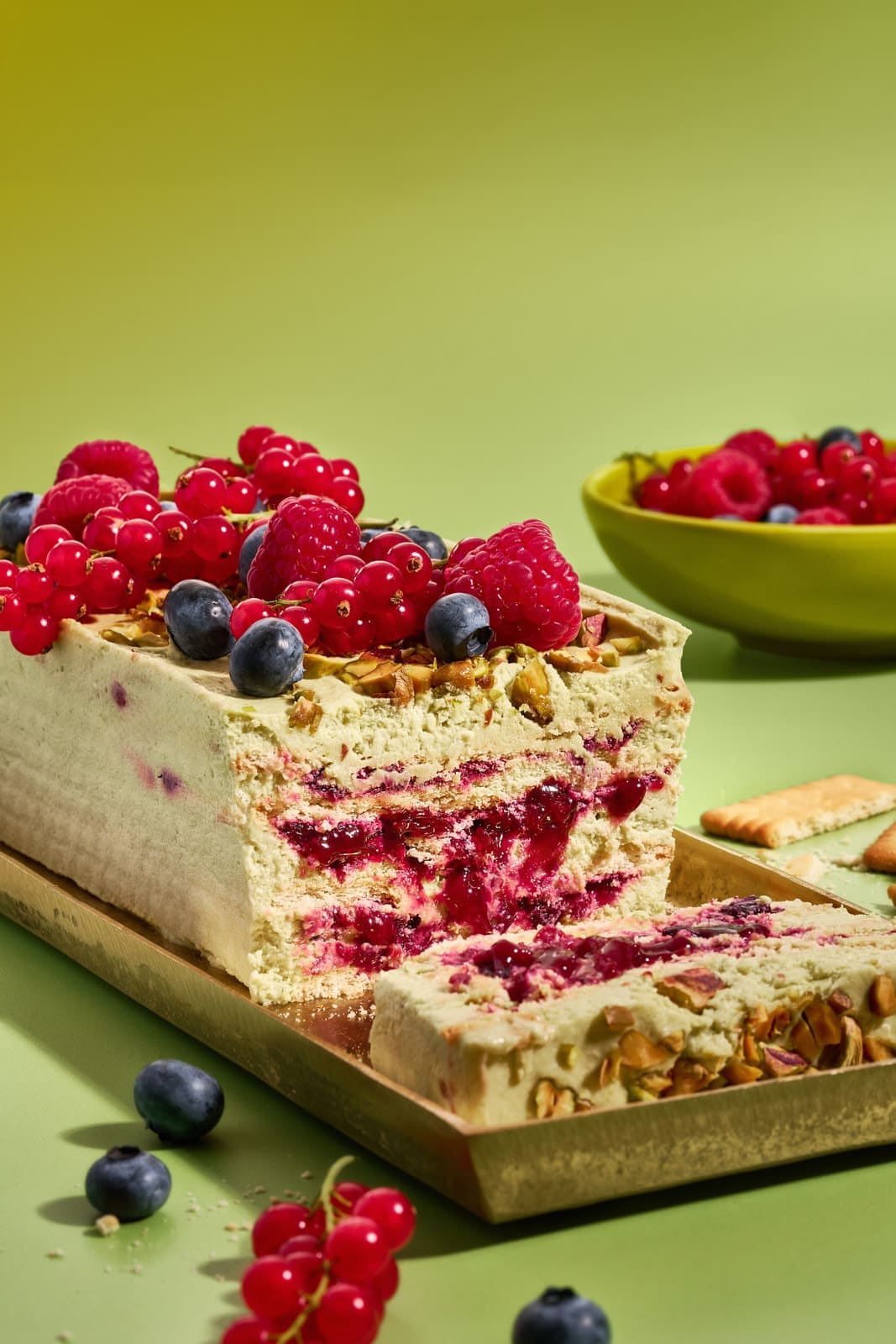 Pistazienkuchen ohne Backen. Cremiger Sommerkuchen mit Waldbeeren aus dem Kühlschrank 2 Angeschnittener Pistazienkuchen ohne Backen, Schnittfläche mit Pistaziencreme-Schichten und Waldbeeren-Kompott, oben frische Beeren