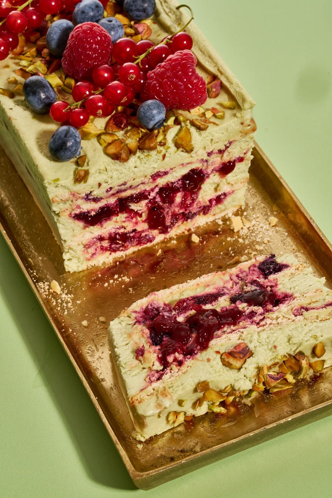 Pistazienkuchen ohne Backen. Cremiger Sommerkuchen mit Waldbeeren aus dem Kühlschrank 7 Cremiger Pistazienkuchen ohne Backen von der Seite, Schichten aus Pistaziencreme und Waldbeeren-Kompott sichtbar