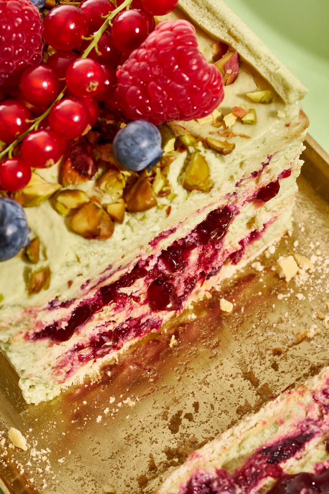 Pistazienkuchen ohne Backen. Cremiger Sommerkuchen mit Waldbeeren aus dem Kühlschrank 3 Nahaufnahme der Schichten aus Waldbeeren-Kompott, Pistaziencreme und weichen Butterkeksen im No-Bake-Kuchen