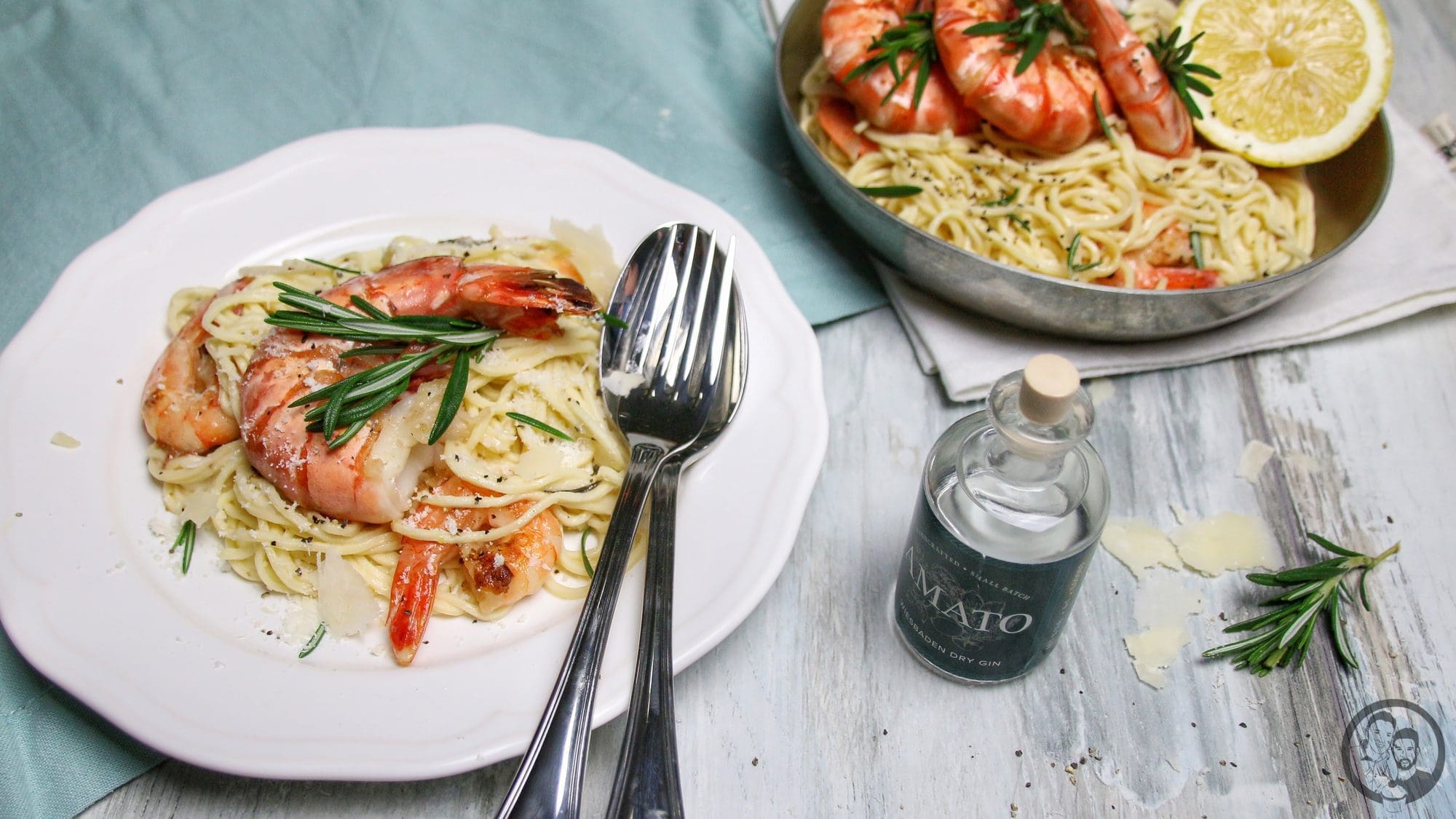 Gedeckter Tisch mit Gin-Zitronen-Pasta und Garnelen, daneben eine Flasche Gin, Zitrone und frischer Rosmarin
