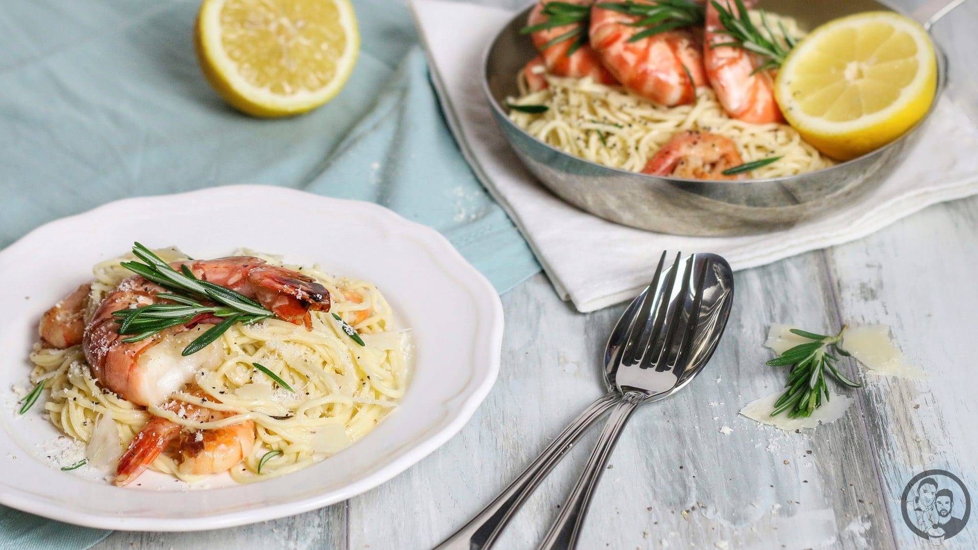 Ein Teller Gin-Zitronen-Pasta mit Garnelen neben der servierten Pfanne, dazu Besteck, Zitronenhälfte und Parmesanspäne