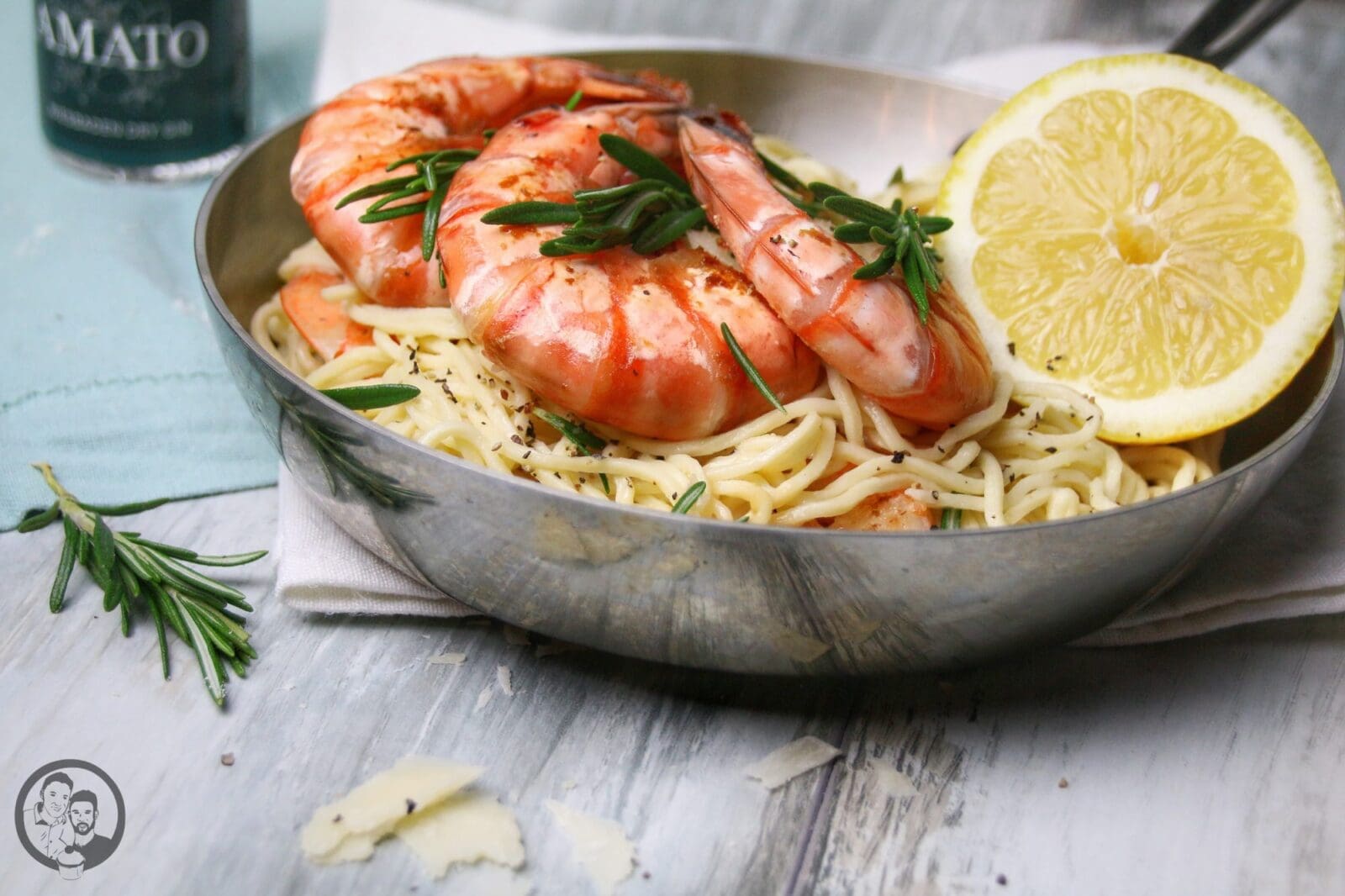 Pasta mit Garnelen in Gin-Zitronen-Sauce in einer Edelstahlpfanne, garniert mit Rosmarin, Pfeffer und einer Zitronenscheibe
